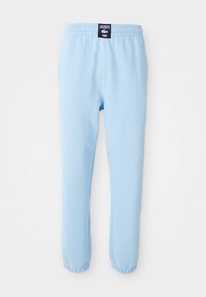 Pantalon de survêtement bleu clair avec poignets et taille élastiques, avec un écusson logo Lacoste Paris noir au centre du dos de la taille.