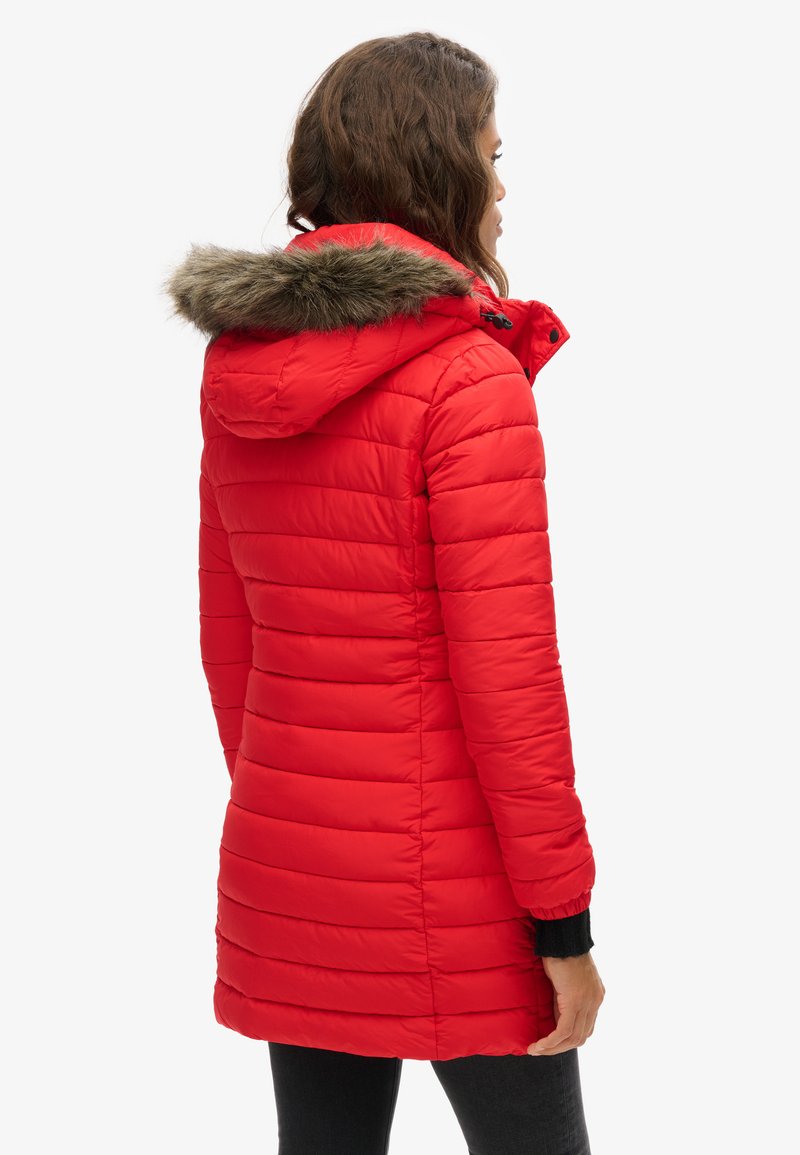 Rode puffer jack met een capuchon en nepbont rand, doorgestikte textuur en elastische manchetten. De jas heeft een slanke pasvorm.