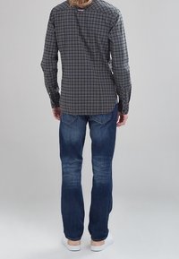 Lange mouwen, geruite shirt in donkergroen en marineblauw, met knopen en een contrasterend ruitpatroon. Draagt met blauwe jeans en witte sneakers.