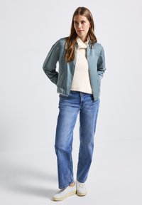 Veste en cuir bleu clair avec un col, associée à un pull texturé crème et un jean bleu. Des baskets blanches complètent la tenue.