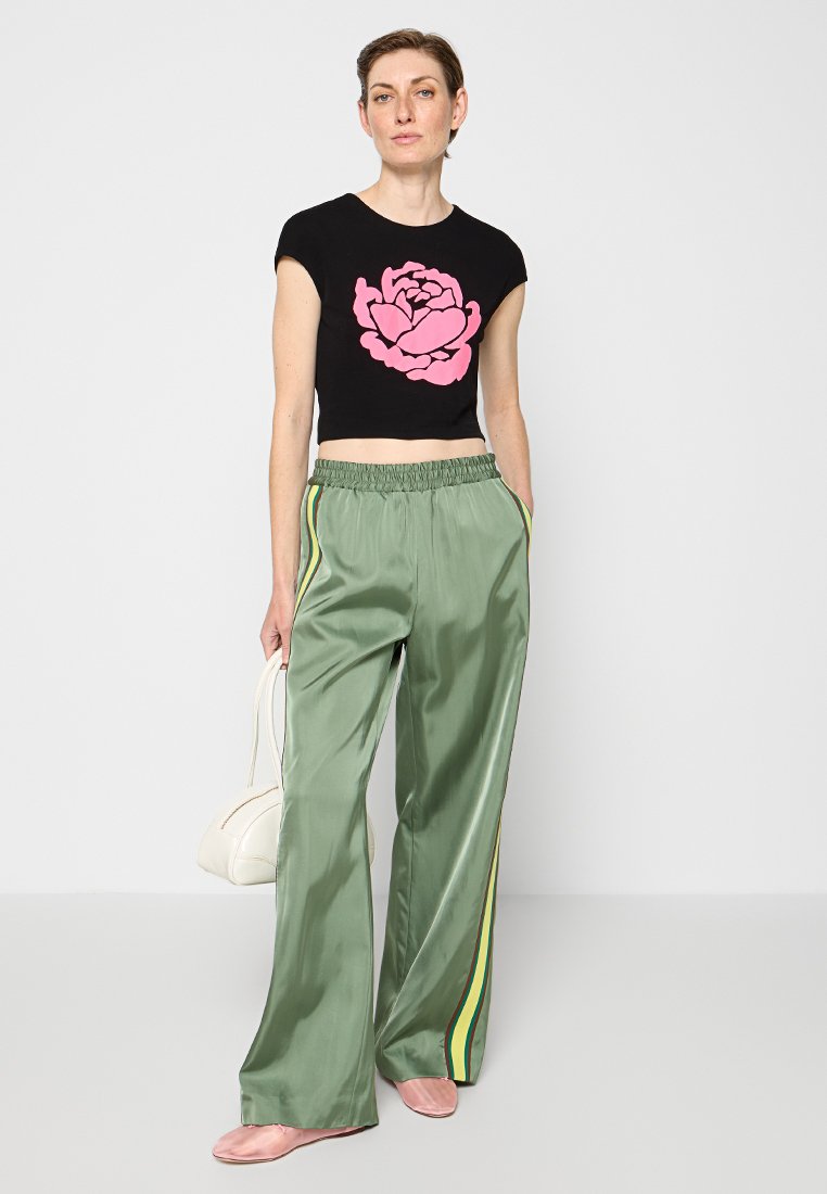 Schwarzes kurzärmeliges T-Shirt mit pinkfarbigem Blumenmotiv, kombiniert mit hellgrünen, satinierten, weit geschnittenen Hosen mit gelben und grünen Seitestreifen.