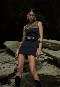 Mini abito in denim nero con una manica in pizzo, orlo finito e chiusura con bottone; abbinato a una borsa a fascia nera e stivali alti fino al ginocchio con lacci.