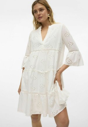 Robe en coton blanche avec un design à niveaux, décolleté en V, manches évasées et motifs floraux brodés. Détail de tissu texturé sur toute la surface.