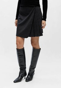 Mørkegrå plisseret nederdel med omslagsdesign, der har lukning med knapper og en struktureret stof. Parret med skinnende sorte knæhøje støvler.