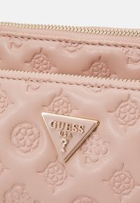 Jasnoróżowy portfel z ekologicznej skóry z wytłaczanym wzorem kwiatowym, z podwójnymi kieszeniami na suwak i złotą trójkątną tabliczką z logo.