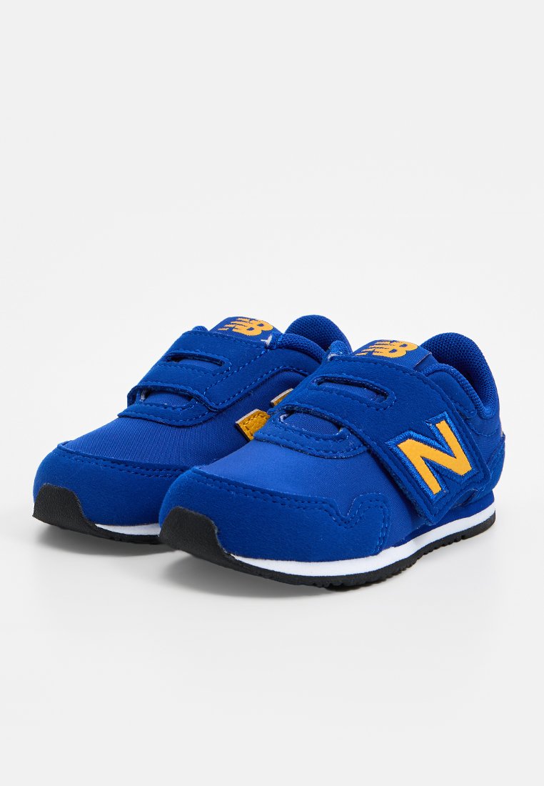 Baskets en velcro bleues en tissu avec une finition texturée. Présentent un logo "N" jaune, une semelle extérieure noire et une semelle intermédiaire blanche.