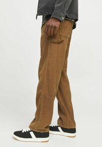 Pantalones de pana marrones con un corte recto, que presentan bolsillos laterales y una tela texturizada. Llevados con zapatillas negras con acentos blancos.