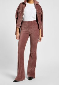 Conjunto de chaqueta de pana y pantalones acampanados en rosa polvo. La chaqueta cuenta con bolsillos frontales y cuello con solapa. El material tiene una textura acanalada.