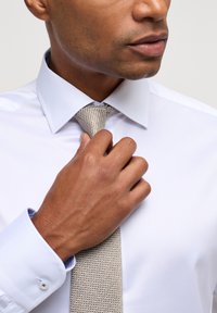 Witte dress shirt met een spread collar, voorzien van een gestructureerde lichtbruine stropdas. De manchetten van het shirt hebben een blauwe patroonaccent.