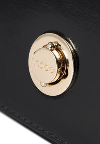 Bolso de cuero sintético negro con un destacado cierre circular dorado con "nöbo" grabado. Textura suave con un sutil detalle de costura.