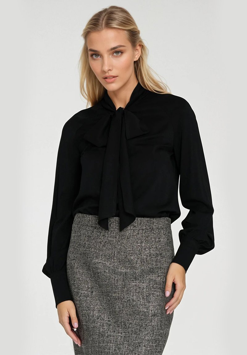 Czarna bluzka z długim rękawem i wiązanym dekoltem, gładki materiał i dopasowany krój, zestawiona z teksturowaną szaro-skalą spódnicą o kroju ołówkowym.
