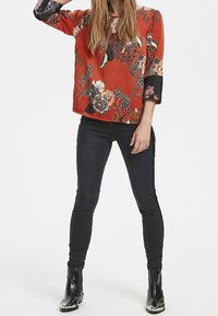 Blusa con motivo floreale rossa a tre quarti, abbinata a jeans skinny neri e stivaletti neri con punta lucida.