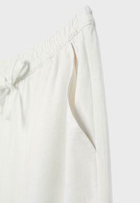 Pantalon en lin blanc avec taille élastique, cordon à l'avant, poche dans la couture latérale et coupe décontractée.
