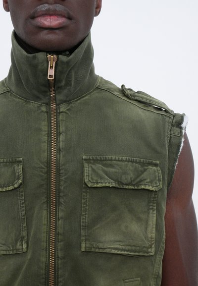 Gilet sans manches vert olive en tissu texturé, avec un col montant, une fermeture éclair à l'avant et deux poches poitrine à rabat.