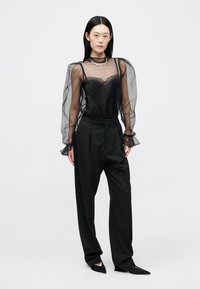 Mustast läbipaistvast kangast pikkade varrukatega pluus, millel on pahkluuni paistetavad varrukad ja pitsist ääris, kombineeritud kõrge vöökohaga mustade pükstega ning teravate mustade madalate kingadega.