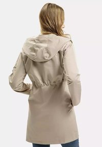 Beżowy płaszcz przeciwdeszczowy z kapturem, z wcięciem w talii, długimi rękawami i gładką teksturą. Posiada detale z guzikami po bokach i długość do połowy uda.