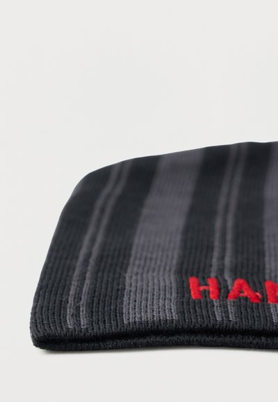 Čierna a sivá pruhovaná pletená čiapka s rebrovanou štruktúrou, zdobená červeným vyšívaným textom. Zložený okraj odhaľuje mäkký, pružný materiál.