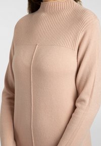 Pull rose clair avec col montant côtelé, corps lisse, détail de couture latérale et manches longues. Fabriqué en tissu doux et texturé.