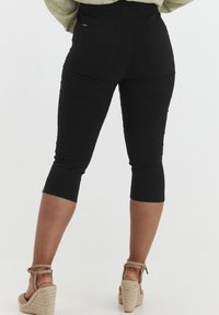Pantaloni capri neri realizzati in tessuto elasticizzato con un design aderente. Presentano tasche posteriori e un orlo che termina appena sotto il ginocchio.