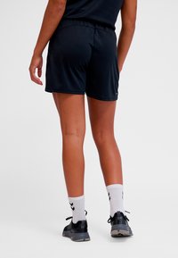 Shorts de sport noirs avec une ceinture élastique, une texture lisse et un détail d'étiquette, accompagnés de chaussettes blanches et de baskets noires.