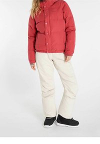 Rote isolierte Steppjacke mit Kapuze, ausgestattet mit einer Knopfleiste und elastischen Bündchen, kombiniert mit beigefarbenen Hosen und schwarzen Winterstiefeln.