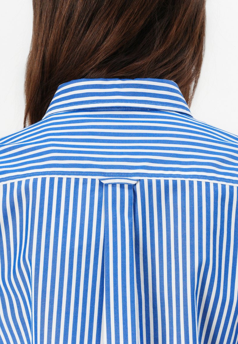 Hemd mit blauen und weißen Streifen. Verfügt über einen strukturierten Kragen und eine Rückenfalte. Hergestellt aus glattem Stoff.