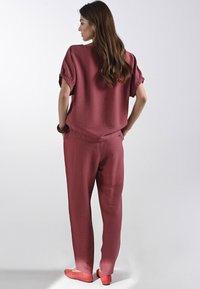 Halenka s nafouknutými rukávy a odpovídající kalhoty z texturované tmavě růžové látky. Slim-fit design s jemným elastickým detailem v pase. Červené baleríny.