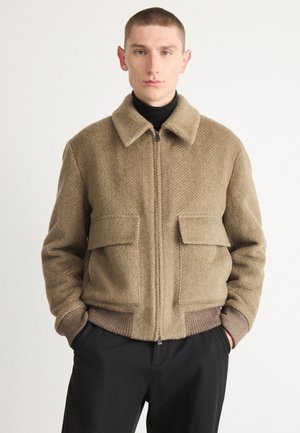 Brun herringbonezip-jacka med krage, två framfickor och ribbade bruna muddar och nederkant. Mjuk textur, avslappnad passform.
