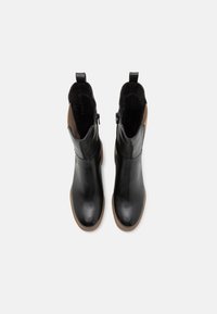Bottines en cuir noir avec une finition lisse, des fermetures éclair sur les côtés et des accents en daim marron, présentant un bout rond et une semelle basse texturée.