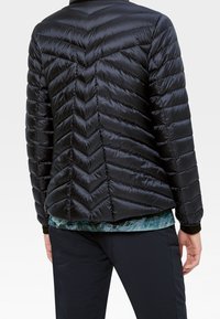 Schwarze Steppjacke mit Zickzack-Steppung, glänzender Textur und taillierter Passform. Sie hat einen hohen Kragen und elastische Bündchen.