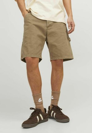 Tan Cargo-Shorts mit Seitentaschen, lockerer Passform und einem Saum, der knapp über dem Knie endet, kombiniert mit braunen Sneakers und gerippten Socken.