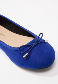 Ballerines bleu en daim avec un bout arrondi, détail en satin avec un nœud et accent métallique. Intérieur lisse pour un confort optimal.