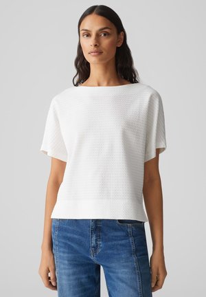 Witte top met korte mouwen, een gestructureerd patroon, ronde halslijn en een relaxte pasvorm. Gecombineerd met blauwe spijkerbroek. Eenvoudig, strak design.