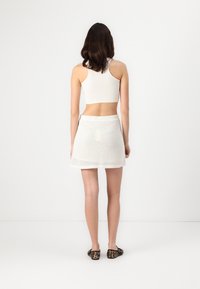 White ribbed tank top paired with a white mesh skirt and leopard print flats. View from the back, showcasing the outfit's simple lines and textures.