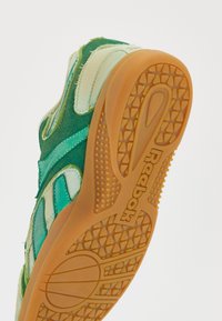Grüner und türkiser Sportschuh mit einer strukturierten Gummisohle, Obermaterial aus Wildleder und Stoff sowie einem auffälligen Reebok-Logo an der Unterseite.