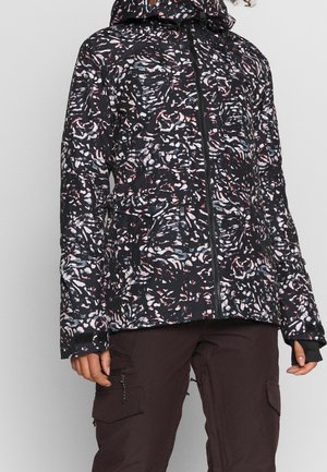 Chaqueta negra con capucha con patrones abstractos en rosa, blanco y azul, combinada con pantalones cargo marrón oscuro con bolsillos con cremallera.