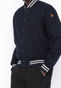 Giacca varsity in lana blu navy con chiusura a bottoni, polsini e orlo a costine rigate, tasche laterali e piccolo logo ricamato sul petto.