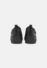 Baskets noires avec un motif texturé de peau de serpent, base en tissu lisse, languettes de tirage et semelle épaisse en caoutchouc.