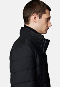Czarna, ocieplana kurtka z wysokim kołnierzem, zamkiem błyskawicznym i żeberkowymi akcentami. Widok z boku podkreśla pikowaną fakturę i wyraźnie zarysowane ramiona.