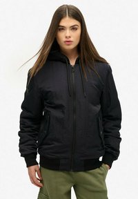 Haut à capuche zippé noir avec une finition texturée, capuche à cordon de serrage et poignets côtelés. Assorti à un pantalon vert olive, doté de poches latérales.