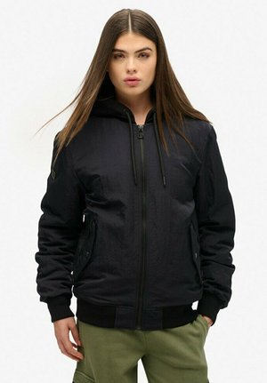 Zwarte hoodie met ritssluiting en een textuurafwerking, met een trekkoordcapuchon en geribde boorden. Gecombineerd met olijfgroene broeken met zijzakken.