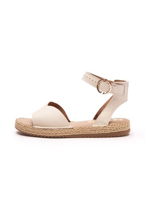Beżowa skórzana sandał z szerokim paskiem na palce, paskiem wokół kostki z metalowym pierścieniem, plecioną juty podeszwą i płaską gumową podeszwą zewnętrzną.