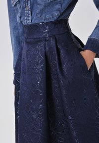 Marineblauwe rok met bloemenpatroon, van een gestructureerde stof en met plooien, met een brede tailleband en zijzakken, gecombineerd met een spijkerblouse.