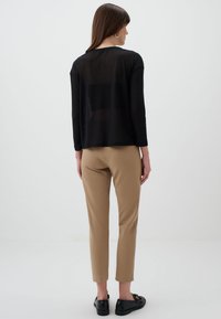 Zwarte sheer lange mouwen top over beige aansluitende broek, met een rechte silhouet en een relaxte pasvorm. Zwarte schoenen maken de outfit af.