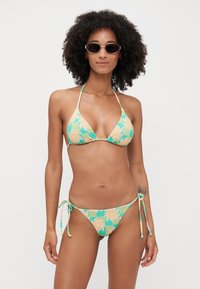 Bikini-Set in Pastellgrün mit Blumenmuster, bestehend aus einem dreieckigen Oberteil mit Bindebändern und einem tief sitzenden Unterteil mit seitlichen Bindebändern. Glatte Stoffstruktur.