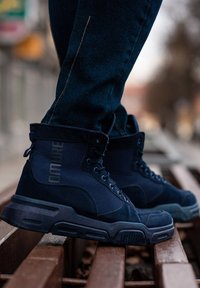 Baskets montantes bleu marine en tissu texturé, avec des lacets ronds et un collier rembourré ; elles disposent d'une semelle en caoutchouc et d'une marque sur le côté.