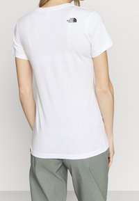 Vit kortärmad T-shirt med rundad halsringning och en tryckt logotyp i svart på övre delen av ryggen. Lätt, slät tyg. Avslappnad passform.