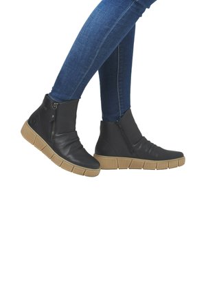 Bottines en cuir noir avec une tige texturée, fermeture éclair sur le côté et semelle en caoutchouc marron dotée d'un design segmenté. Portées avec un jean bleu.