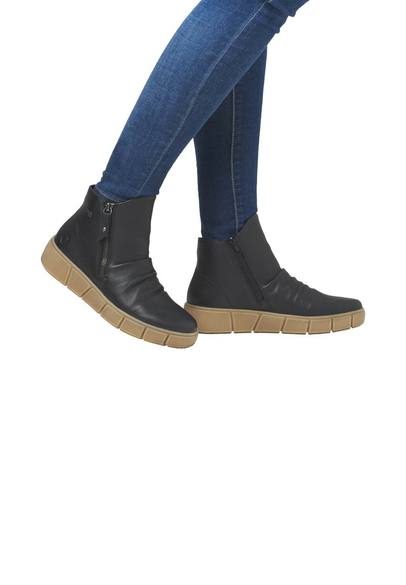 Bottines en cuir noir avec une tige texturée, fermeture éclair sur le côté et semelle en caoutchouc marron dotée d'un design segmenté. Portées avec un jean bleu.