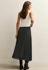 Black pleated skirt with white polka dots, paired with a white tank top and black heeled boots. Smooth fabric, mid-length design.